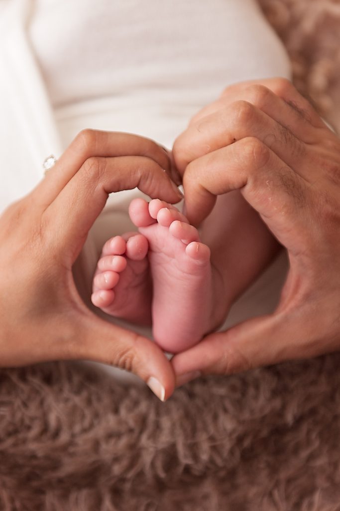 Natural Newborn photography image of tiny baby feet held by their parents hands made in a heart shape by Horsham Photographer