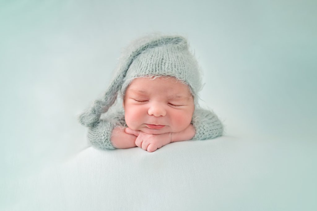 newborn baby boy sleeping on folded arms in a mint green knitted hat and romper on a mint green backdrop, Horsham